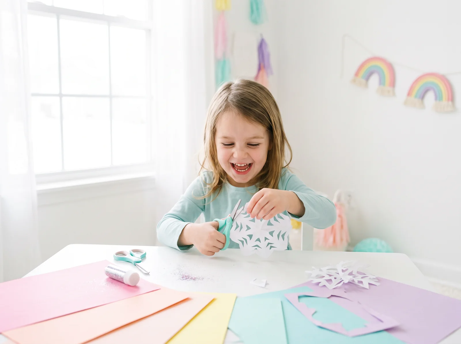 A young child carefully cutting a paper snowflake at the kitchen table.